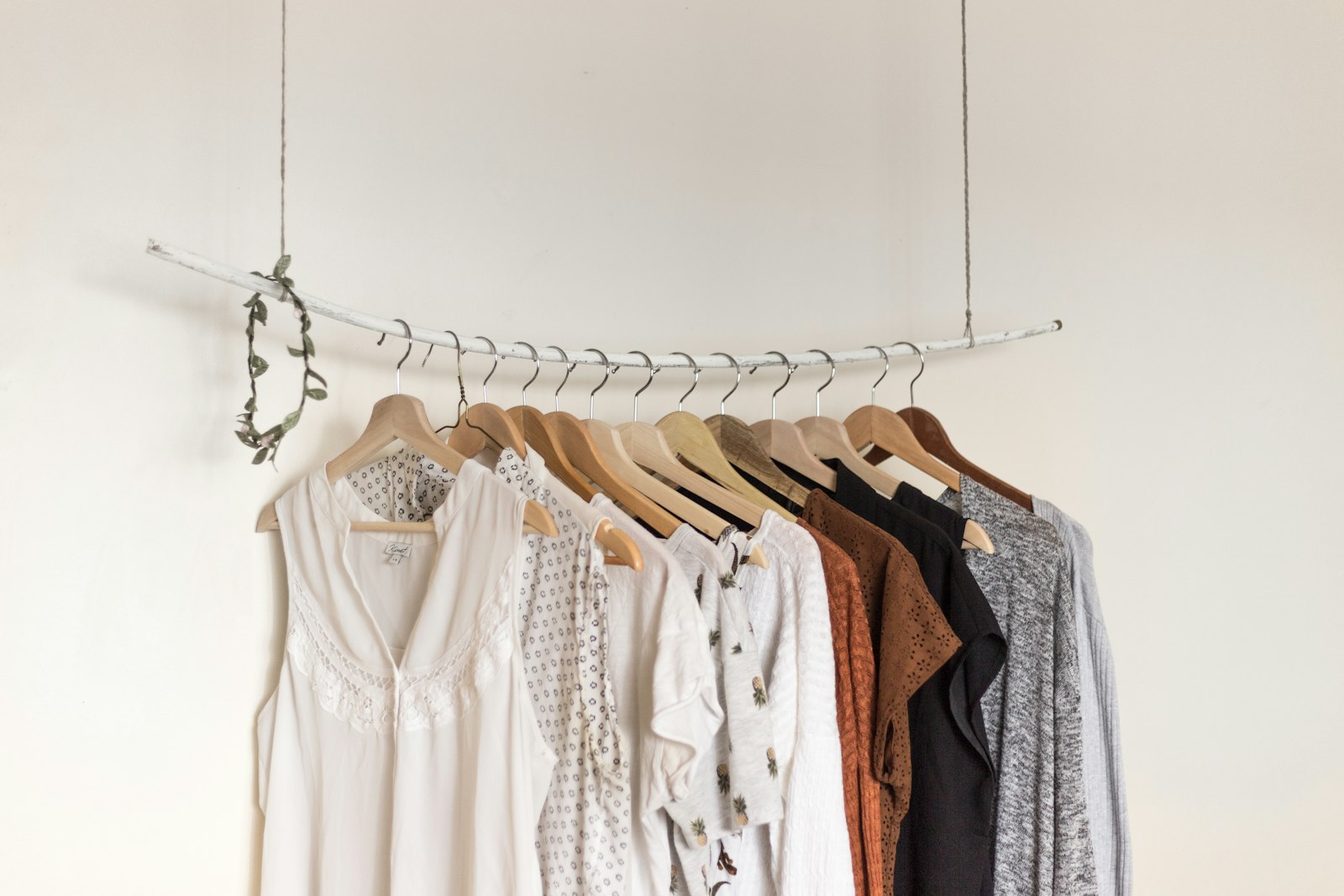 Kleding aan houten hangers aan een eenvoudig rek tegen een witte muur